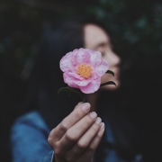 A girl extending a large pink flower toward the camera.