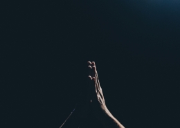 hands praying against a black background.